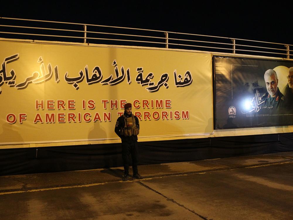 Iran is seeking to detain President Trump over the U.S. killing of top Iranian military commander Qassem Soleimani. Here, an Iraqi fighter stands in front of a banner at the site of the drone strike at Baghdad International Airport.