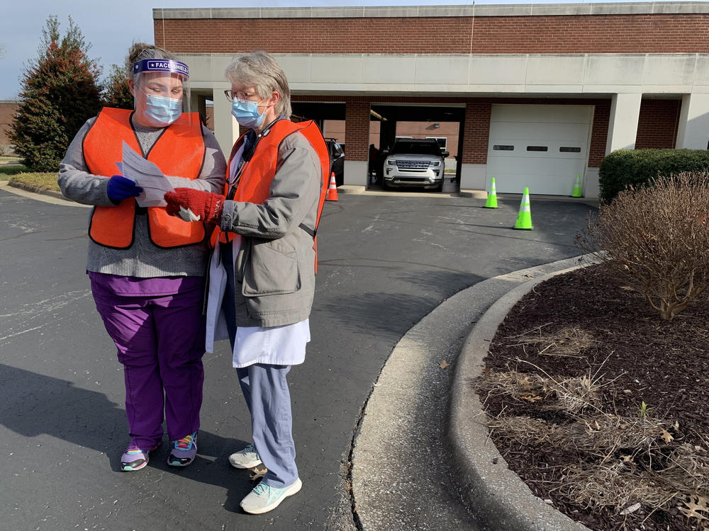 Dr. Lorraine MacDonald (right), the medical examiner in Rutherford County, Tenn., talks to a public health worker giving shots at the county's mass vaccination site, located in an old State Farm operations center. MacDonald says if people are able to sign up online, and their cars make it to the front of the line, health workers don't question whether they qualify.