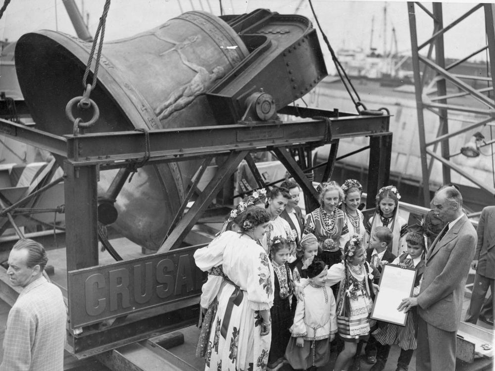 A group of former displaced persons helps load the Freedom Bell aboard a Navy transport vessel in Brooklyn, N.Y., on Oct. 9, 1950. One of the children, Eva Zandler, 8, originally from Poland, presents a scroll — to be enshrined in the Freedom Bell's tower in Berlin — to Frederick Osborn, the New York City chairman of the Crusade for Freedom.