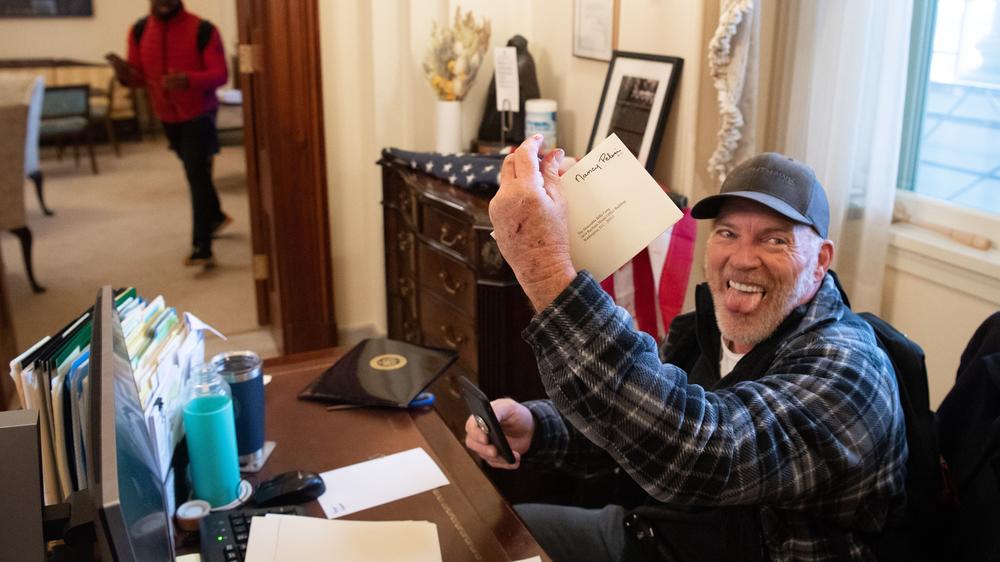 Richard Barnett holds a piece of mail as he sits inside the office of House Speaker Nancy Pelosi after rioters breached the U.S. Capitol. He bragged about leaving a note containing a sexist slur for Pelosi.