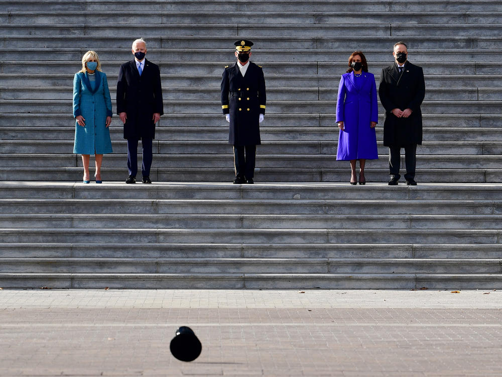 High winds blow a hat by as President Biden, first lady Jill Biden, Vice President Harris and second gentleman Douglas Emhoff walk down the steps of the Capitol.