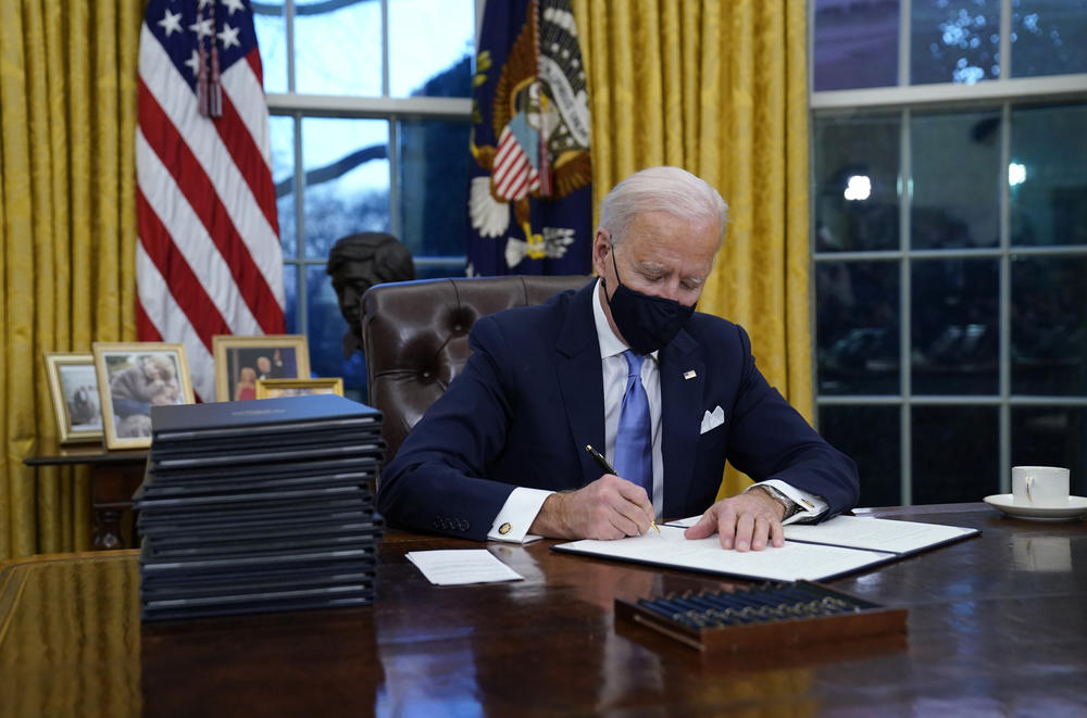 President Biden signs his first executive action in the Oval Office on Wednesday afternoon.