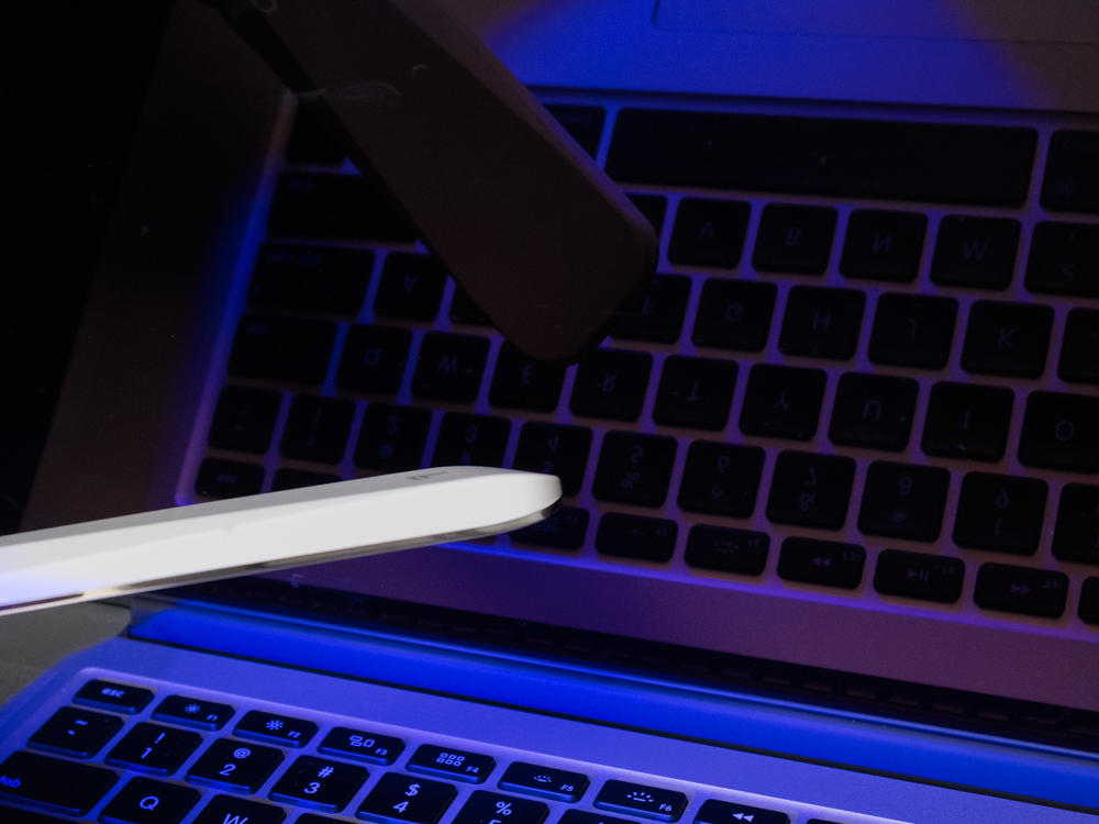 A handheld ultraviolet-C wand is waved over the surface of a computer keyboard.