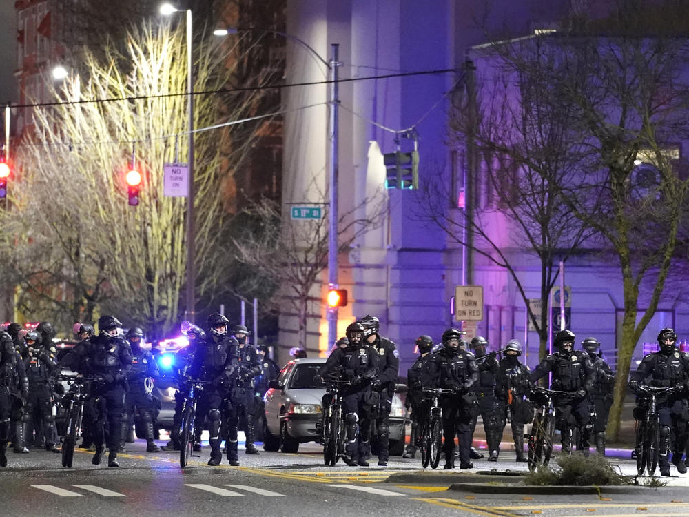 Police and other law enforcement officials stand in a line as protesters approach Sunday in the street in front of the City-County Building in Tacoma, Wash.