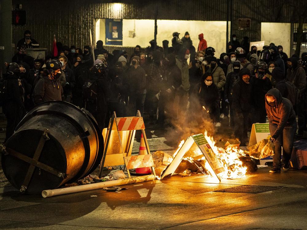 A demonstrator adds fuel to a burning barricade in an intersection in downtown Tacoma during an anti-police protest Sunday.