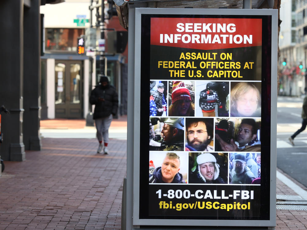 A sign on a bus shelter asks the public for information about people involved in the Jan. 6 Capitol insurrection.