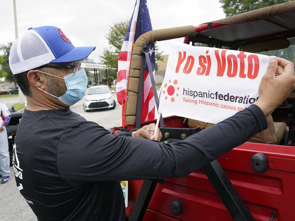 John Gimenez attaches a flag to his vehicle during an event hosted by the Hispanic Federation to encourage voting in the Latino community Sunday, Nov. 1, 2020, in Kissimmee, Fla. The Hispanic Federation is a non-partisan organization.