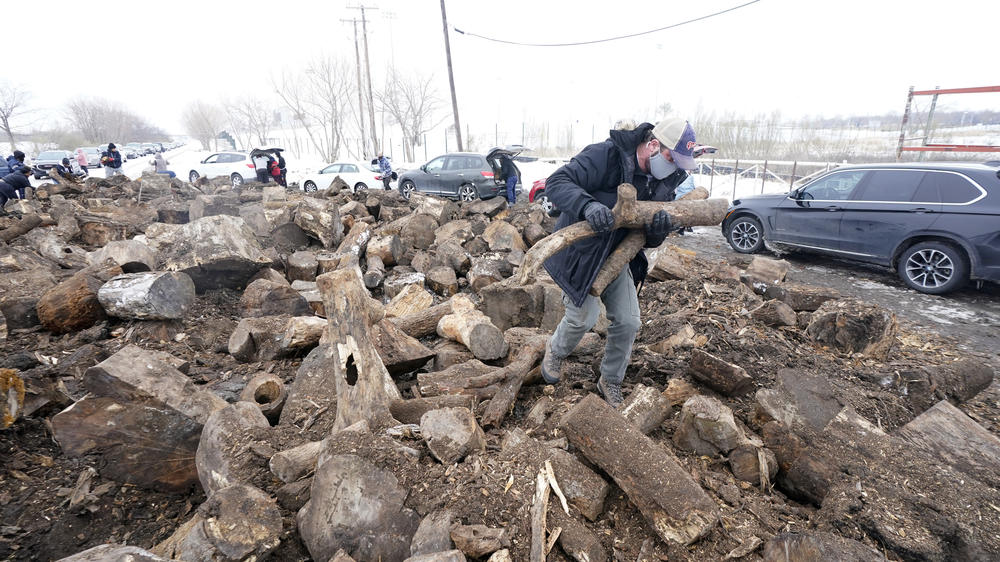 People collect firewood with others from a wood heap opened to the public on Wednesday in Dallas, as cold and snow have shut off power and left many homes around the state frigid.