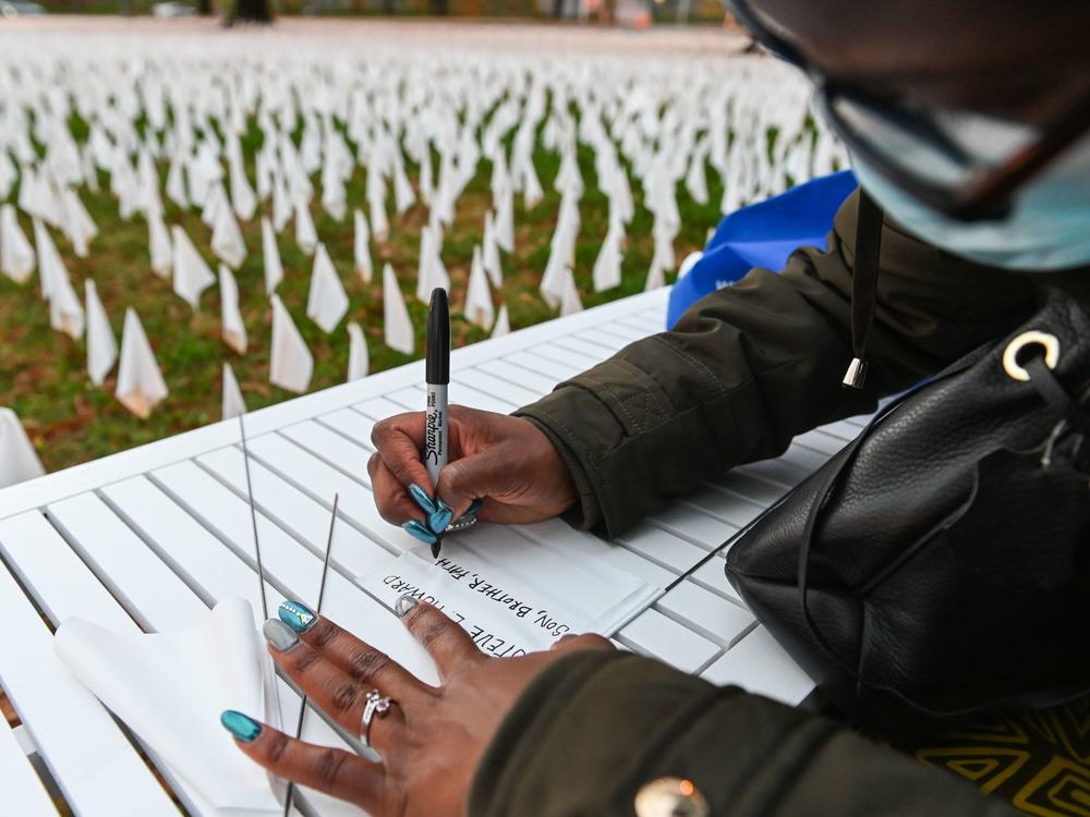 Patrice Howard writes on white flags before planting them to remember her recently deceased father and close friends in November at 