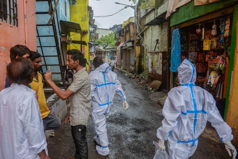 Health workers in personal protective gear walk through a lane after conducting a COVID-19 screening in Mumbai's Dharavi slum on August 11, 2020. After the bubonic plague epidemic, Mumbai hoped to bring an end to congested slums — but that did not happen.