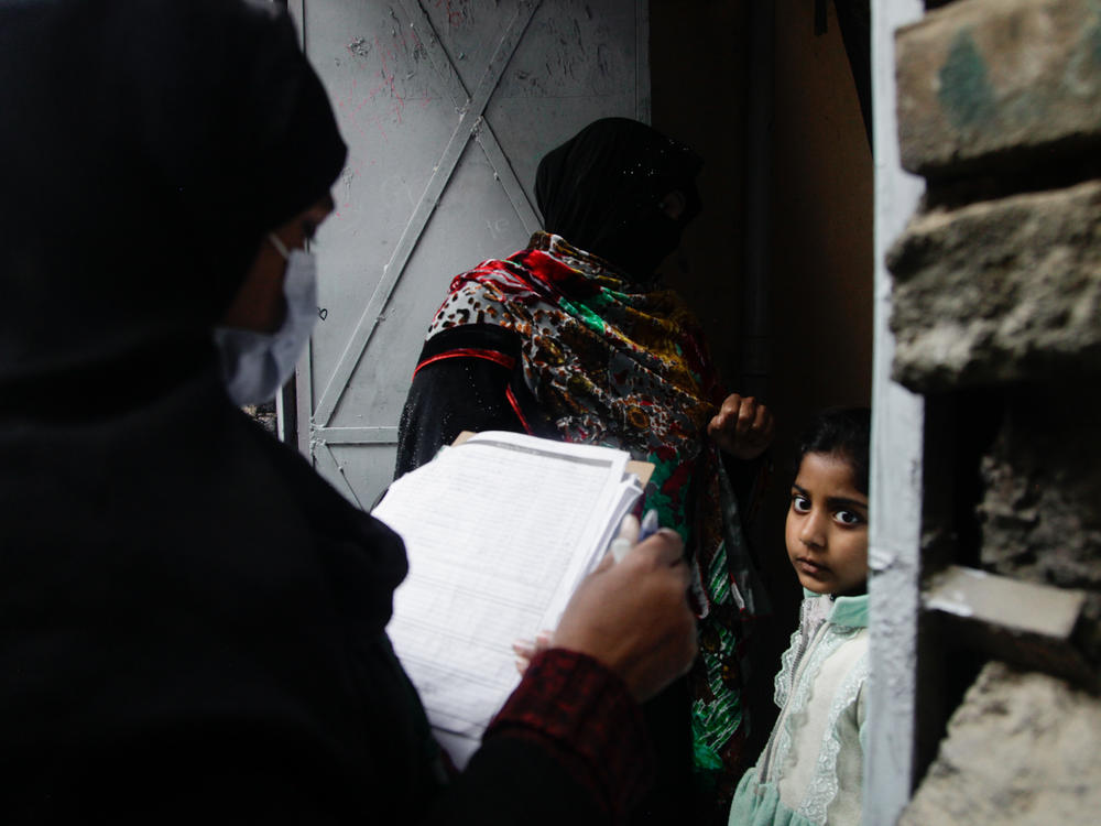 Polio vaccinator Zeenat Parveen, holding the clipboard, and a volunteer go door-to-door to reach children in Rawalpindi, a city near the Pakistani capital of Islamabad.