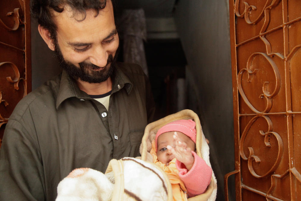 A father holds his son, who was vaccinated two days earlier, as the health workers who'd administered the vaccine return for a follow-up check.