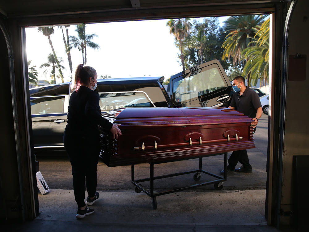 Embalmer and funeral director Kristy Oliver (left) and funeral attendant Sam Deras load the casket of a person who died after contracting COVID-19 into a hearse in El Cajon, Calif. People who work in hospitals and in funeral homes are witnesses to the loss than many Americans can avoid.