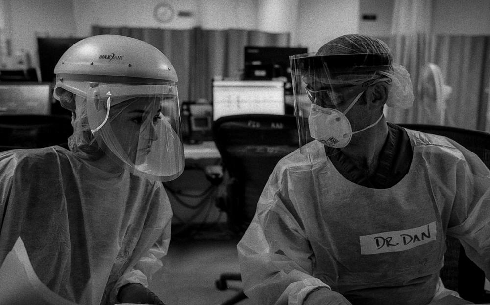 Drs. Katie Ross and Dan Dworkis discuss the care of several patients in the emergency department's COVID-19 unit. The doctors' muffled voices are hard to hear over the sound of air filtration units humming and monitors alarming.