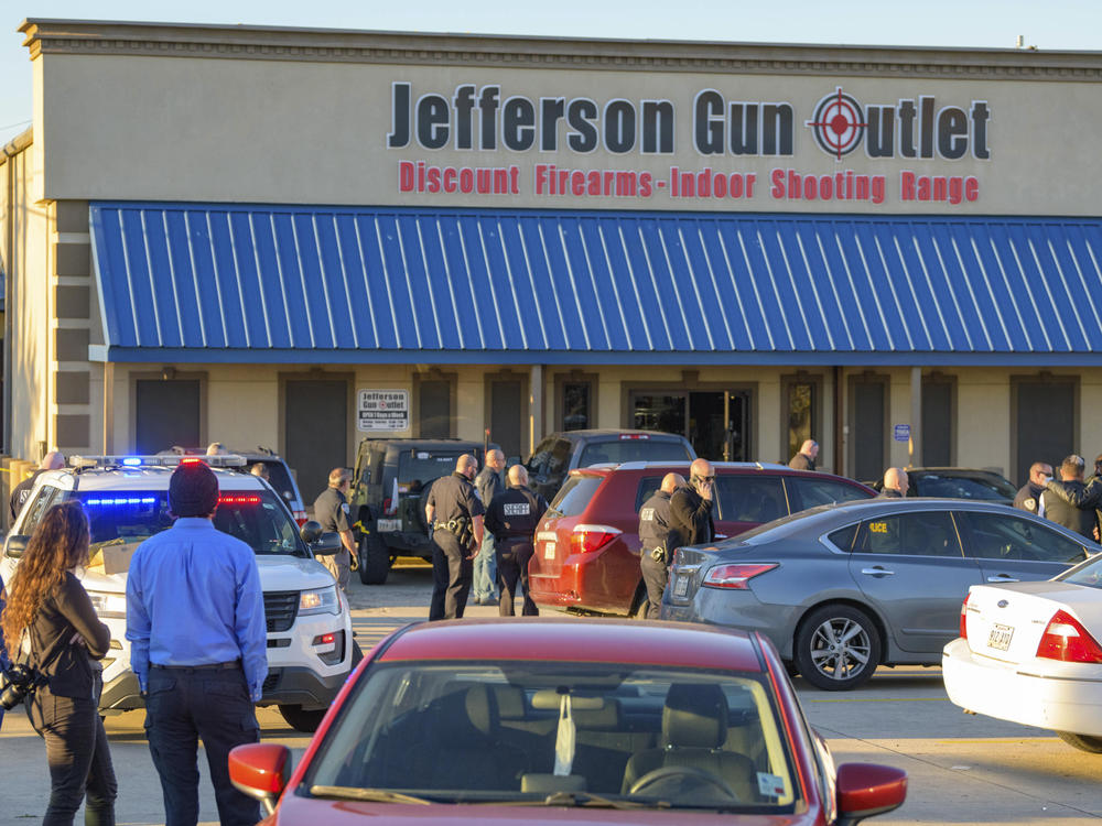 Bystanders gather at the scene of a multiple fatality shooting at the Jefferson Gun Outlet in Metairie, La., Saturday.