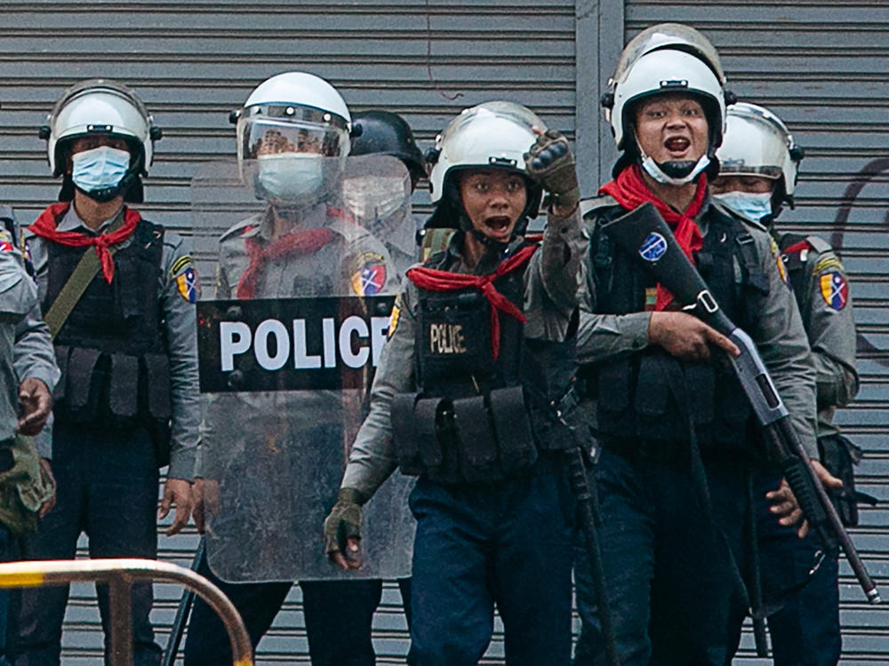 Police gesture toward protesters as security forces crack down on demonstrations against the military coup in Yangon on Sunday. The United Nations says at least 18 protesters were killed Sunday, the deadliest day yet since the military took power earlier this month.
