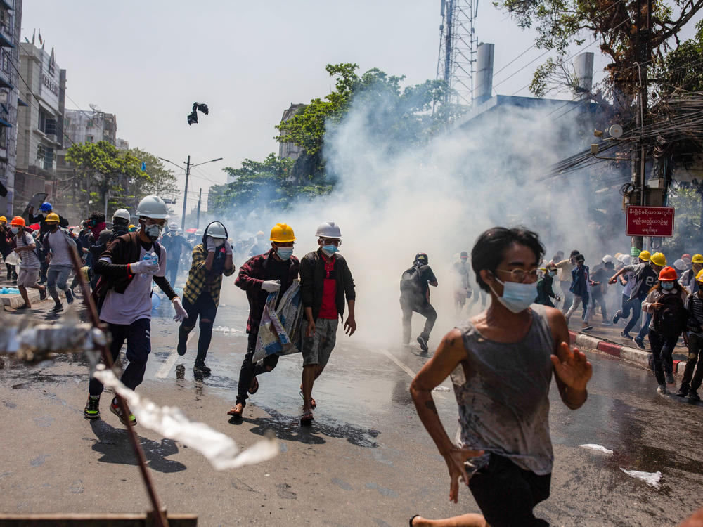 Anti-junta protesters run from teargas fired by police during a demonstration in Yangon on Monday. At least 18 people were killed over the weekend as Myanmar police reportedly used live ammunition against protesters.