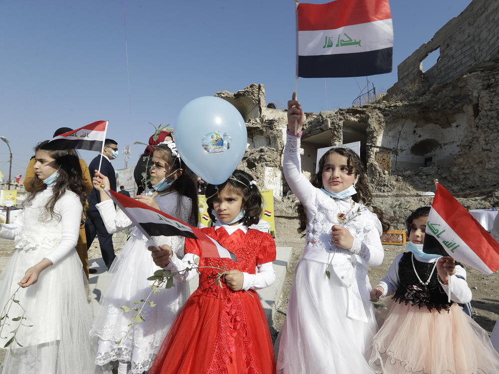 Children in their festive garment wave Iraqi flags as they arrived to join Pope Francis at Hosh al-Bieaa Church Square, in Mosul.