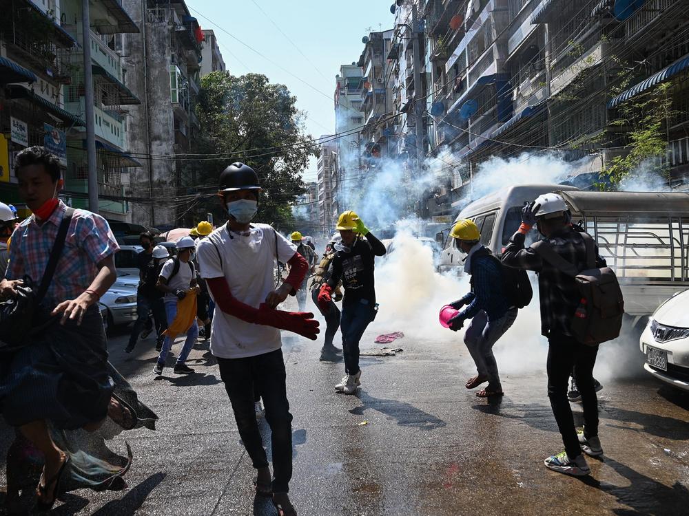 Protesters in Yangon run from police Sunday after they fire tear gas during a demonstration against the military coup.