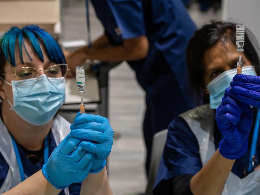 Two health care workers prepare syringes with AstraZeneca's COVID-19 vaccine in London Monday. A U.K. study will expose volunteers to the coronavirus and could help development of future vaccines.