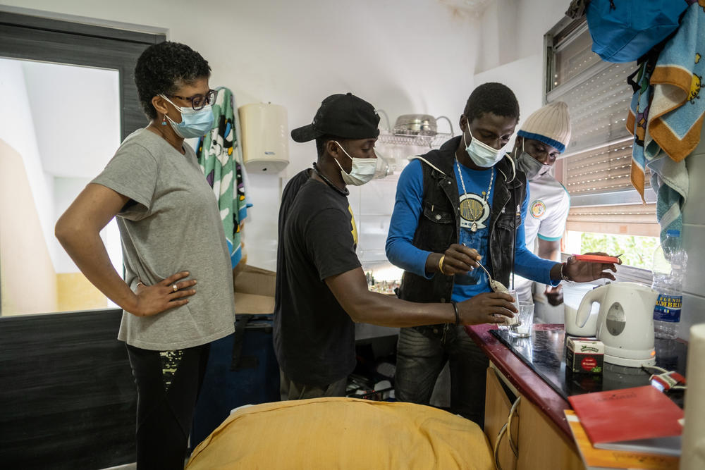 Alexandra Christina Kouhiho, left, a volunteer Somos Red stands by as migrants prepare tea in the afternoon at a hostel the solidarity group has rented for some migrants to live in, after they were found living on the streets.