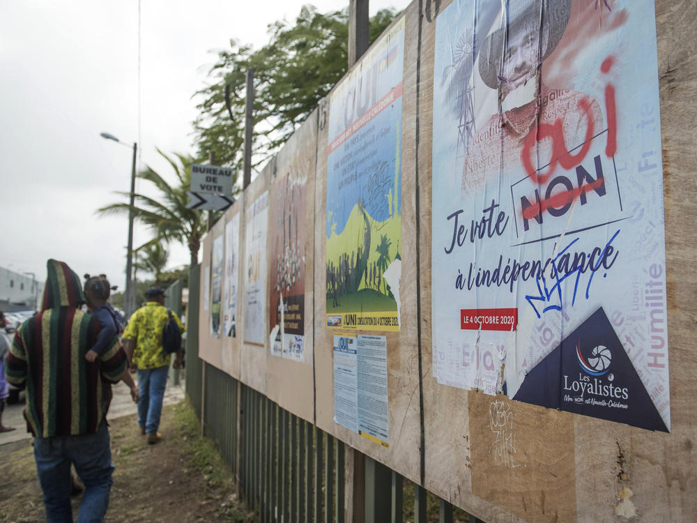 People arrive at a polling station for a referendum and walk past political posters in Nouméa, New Caledonia, in October.