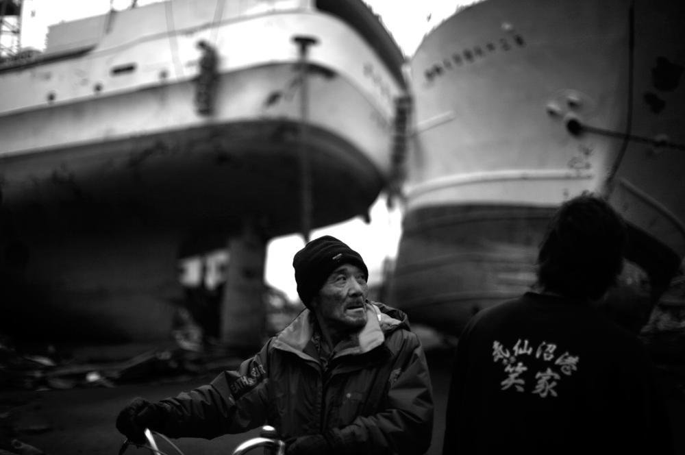 A Japanese man walks his bike between two massive trawlers that were thrown ashore in Kesennuma, Japan.