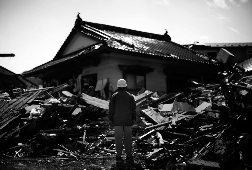 A man looks at one of the few buildings remaining upright — sort of — in Noda, a week after the disaster.