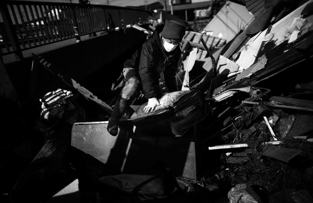 A woman climbs out of the ruins of her home, which was washed beneath a bridge in Noda in northeastern Japan on March 18, 2011.