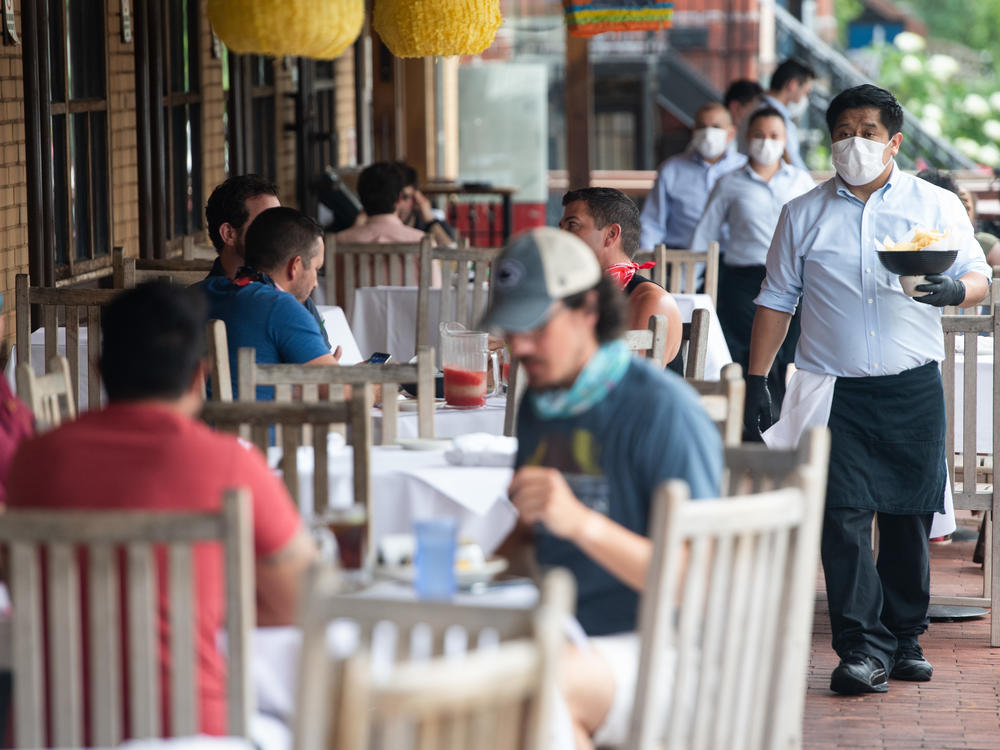 A waiter wearing a mask and gloves delivers food to a table to customers seated at an outdoor patio at a restaurant in Washington, D.C. in May.