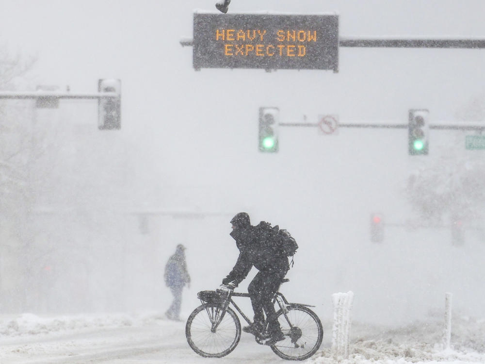 People cross the road as a sign warns of heavy snow on Sunday in Denver, Colo. A winter storm closed roads, impacted flights, and knocked out power in Arizona, Wyoming, Nebraska, and Colorado through the weekend.