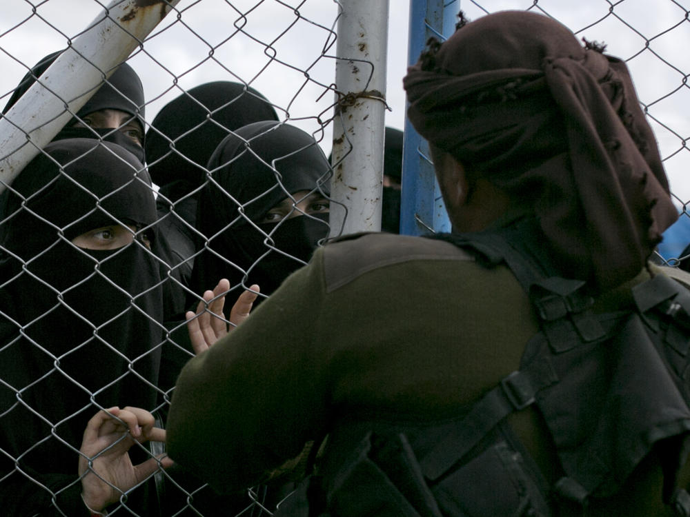 In this March 31, 2019, photo, women speak to guards at the gate that closes off the section for foreign families who lived in the Islamic State's so-called caliphate, at al-Hol camp in Hasakeh province, Syria.