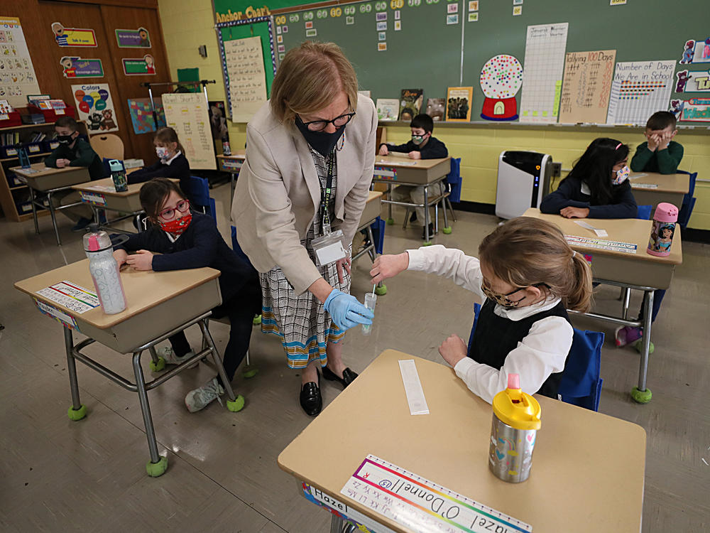 A student gives her coronavirus swab to Helenann Civian, the principal of South Boston Catholic Academy in Boston in January. The White House announced $10 billion to expand testing in K-12 schools.