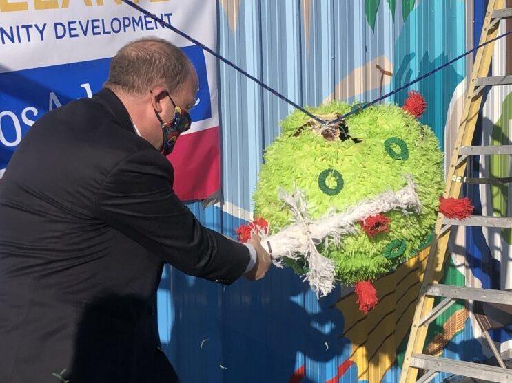 Gov. Jared Polis takes a swing at a piñata representing the COVID-19 virus, during a visit to the Adelante Community Development Clinic at Mile High Flea Market in Henderson, Colo. Feb. 26.