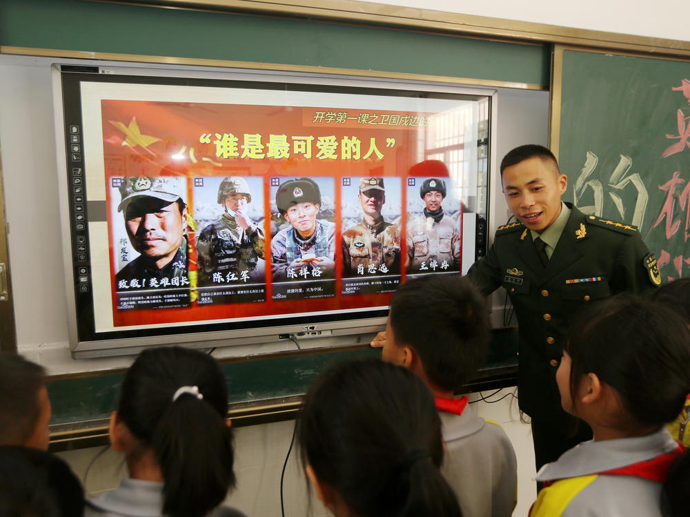 A paramilitary police officer talks next to a screen showing frontier soldiers of the People's Liberation Army during an event at a primary school in Wuzhishan, Hainan province, China, on Feb. 22. On the screen are (L-R) Qi Fabao, who was seriously wounded in the border clash with Indian troops in June last year, and four who were killed: Chen Hongjun, Chen Xiangrong, Xiao Siyuan and Wang Zhuoran.