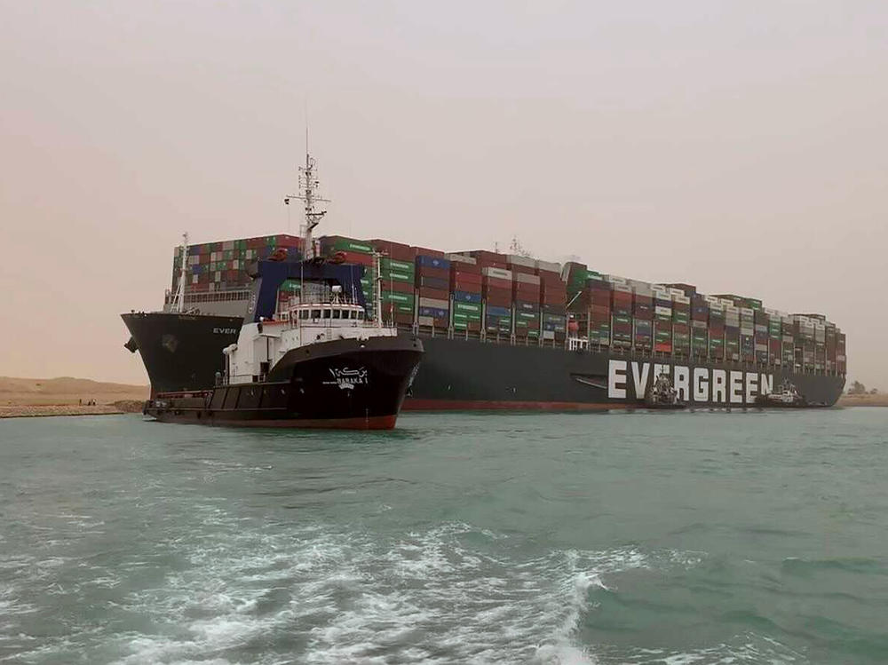 A boat navigates in front of a massive cargo ship that sits grounded after it turned sideways in Egypt's Suez Canal, blocking traffic in a crucial East-West waterway for global shipping. An Egyptian official warned Wednesday it could take at least two days to clear the ship.