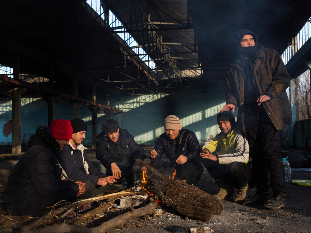 Afghan Morteza Mohammadi (center-left) and his companions sit around a fire in the former Krajina Metal factory in Bihac, Bosnia-Herzegovina, near the Croatian border, discussing possible border crossing strategies related to the weather and time.
