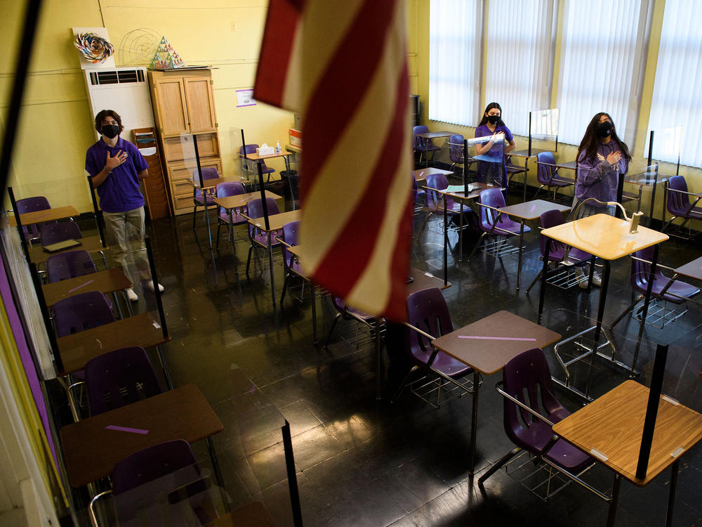 Students stand for the Pledge of Allegiance as they return to in-person learning at St. Anthony Catholic High School in California on March 24. Masks and physical distancing are proving to have some major public health benefits, keeping people from getting all kinds of illnesses, not just COVID-19. But it's unclear whether the strict protocols would be worth the drawbacks in the long run.