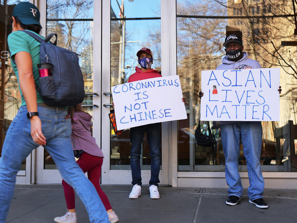 Cameron Hunt and his father, Calvin Hunt, hold signs of support on Tuesday outside the West 43rd Street apartment building in Manhattan where a man physically and verbally attacked a 65-year-old Asian American woman on Monday in an incident that police are investigating as a hate crime.