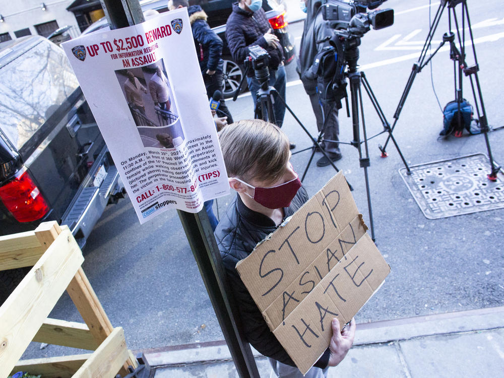 A man holds a sign after an Asian American anti-violence press conference Tuesday outside the building where a 65-year-old Asian woman was  attacked in New York City. Police said Wednesday that Brandon Elliot, 38, had been arrested and charged with crimes that include assault as a hate crime.