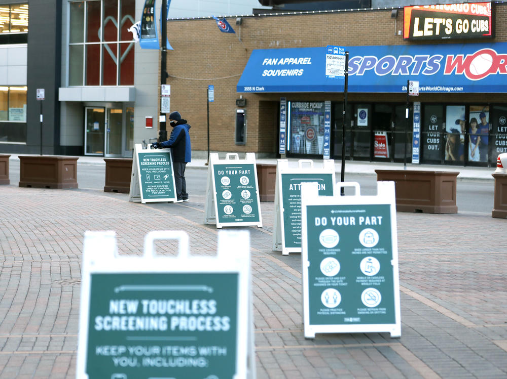 A Wrigley Field employee puts up cautionary signs outside of the ballpark on Opening Day for the Chicago Cubs. Baseball teams are implementing safety measures and social distancing rules as they welcome back fans.