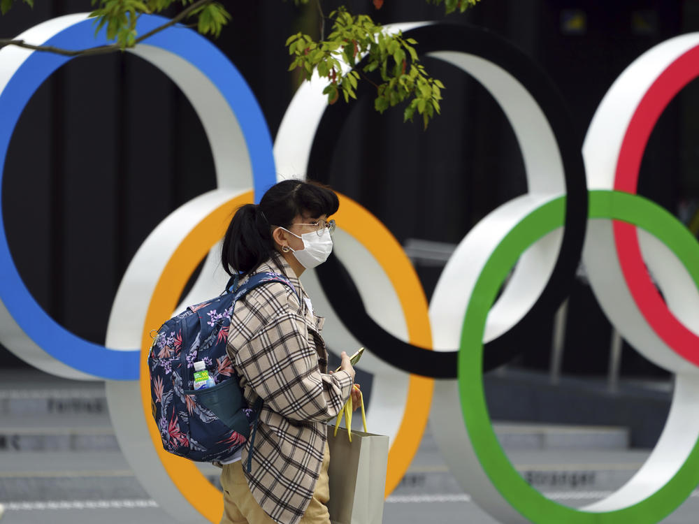 A woman wearing a protective mask to help curb the spread of the coronavirus walks in front of he Olympic Rings on Tuesday in Tokyo. North Korea says it will not attend the games over COVID-19 fears.