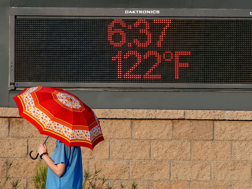 A pedestrian using an umbrella to get some relief from the sun walks past a sign displaying the temperature on June 20, 2017, in Phoenix.