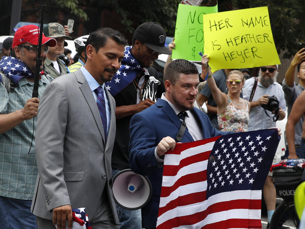 Far-right extremist Jason Kessler (center) walks to the White House in 2018 on the first anniversary of the Unite the Right rally. In the background, a protester holds a sign invoking the name of Heather Heyer, the woman killed in the 2017 rally in Charlottesville, Va.
