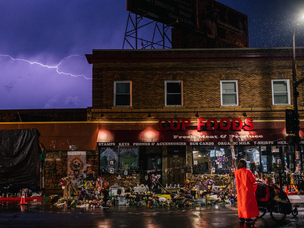 A woman stands with her baby while viewing memorials dedicated to George Floyd in front of the entrance of Cup Foods, the site where George Floyd died.