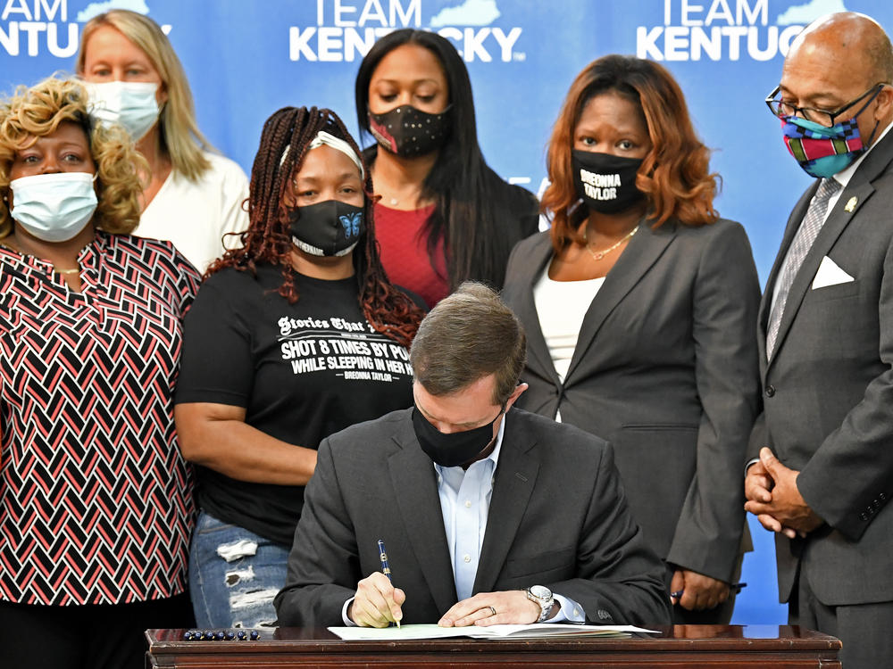 Kentucky Gov. Andy Beshear signs a bill on Friday limiting the use of no-knock warrants statewide. The governor was surrounded by members of Breonna Taylor's family including her mother, Tamika Palmer (standing behind Beshear at left).