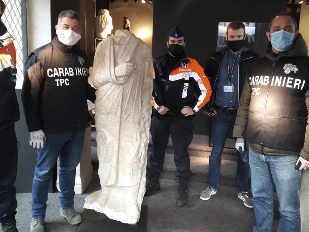 Carabinieri (Italian paramilitary police) officers of the art squad's archaeological unit pose with a headless Roman statue wearing a draped toga in Brussels on Wednesday, Feb. 3, 2021.