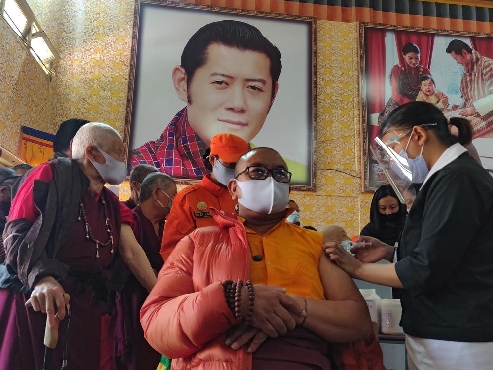 A health worker vaccinates a Buddhist monk sitting in front of a portrait of Bhutanese King Jigme Khesar Namgyel Wangchuck at a secondary school in Bhutan on March 27, the first day of the country's vaccination campaign. Less than two weeks later, health officials said 93% of eligible adults had received their first dose of a COVID-19 vaccine.