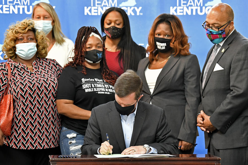 Kentucky Gov. Andy Beshear signs a bill enacting a partial ban on no-knock warrants, as Breonna Taylor's mother, Tamika Palmer, stands to his right.