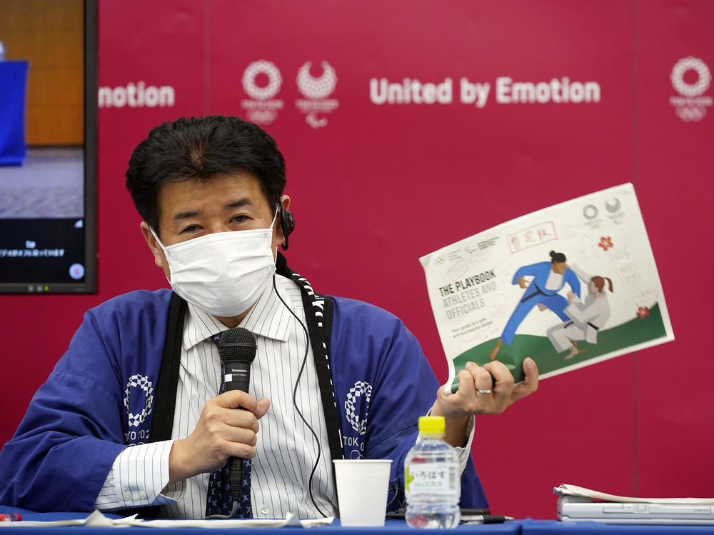 Tokyo Games Delivery Officer Hidemasa Nakamura holds a sample of an updated version of the playbook during a news briefing on Wednesday.